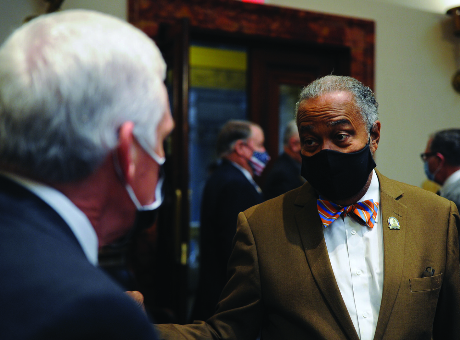Two men wearing masks and suits talking to each other.