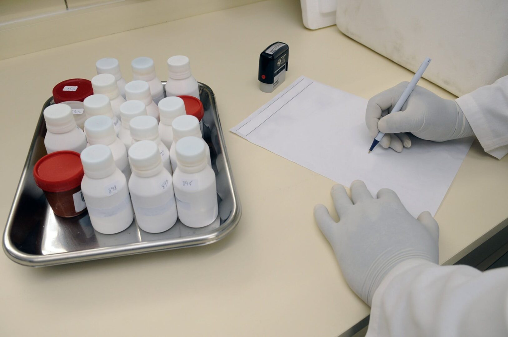 A person writing on paper next to many pills.